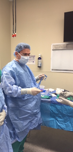 A surgeon in blue scrubs and mask holding surgical instruments.